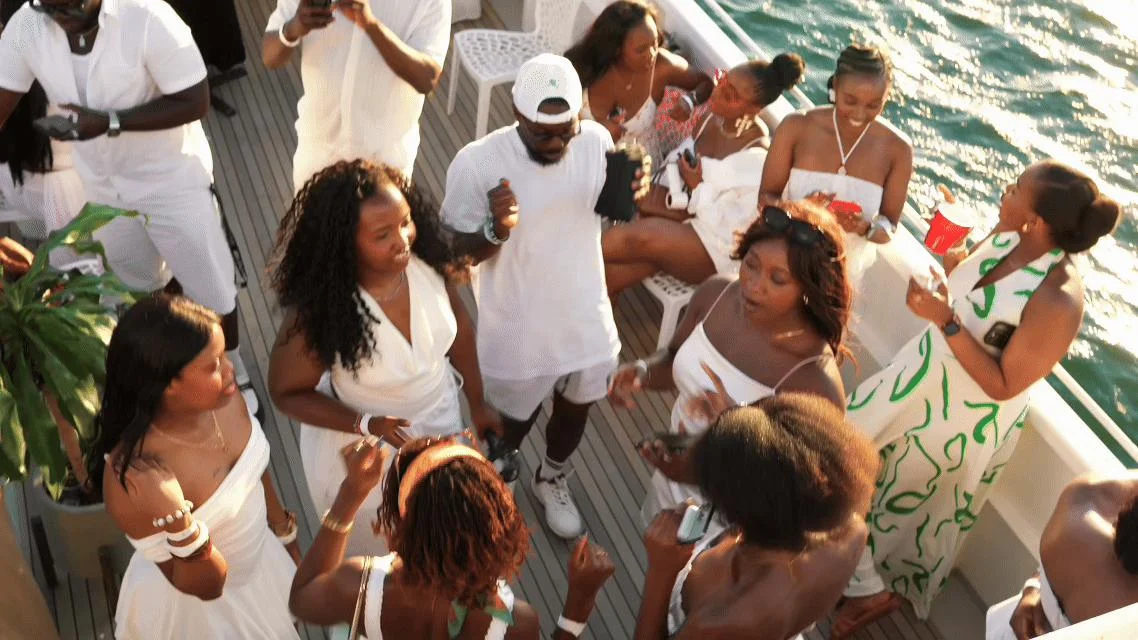 Guests dressed in white gathered on a yacht beside the water